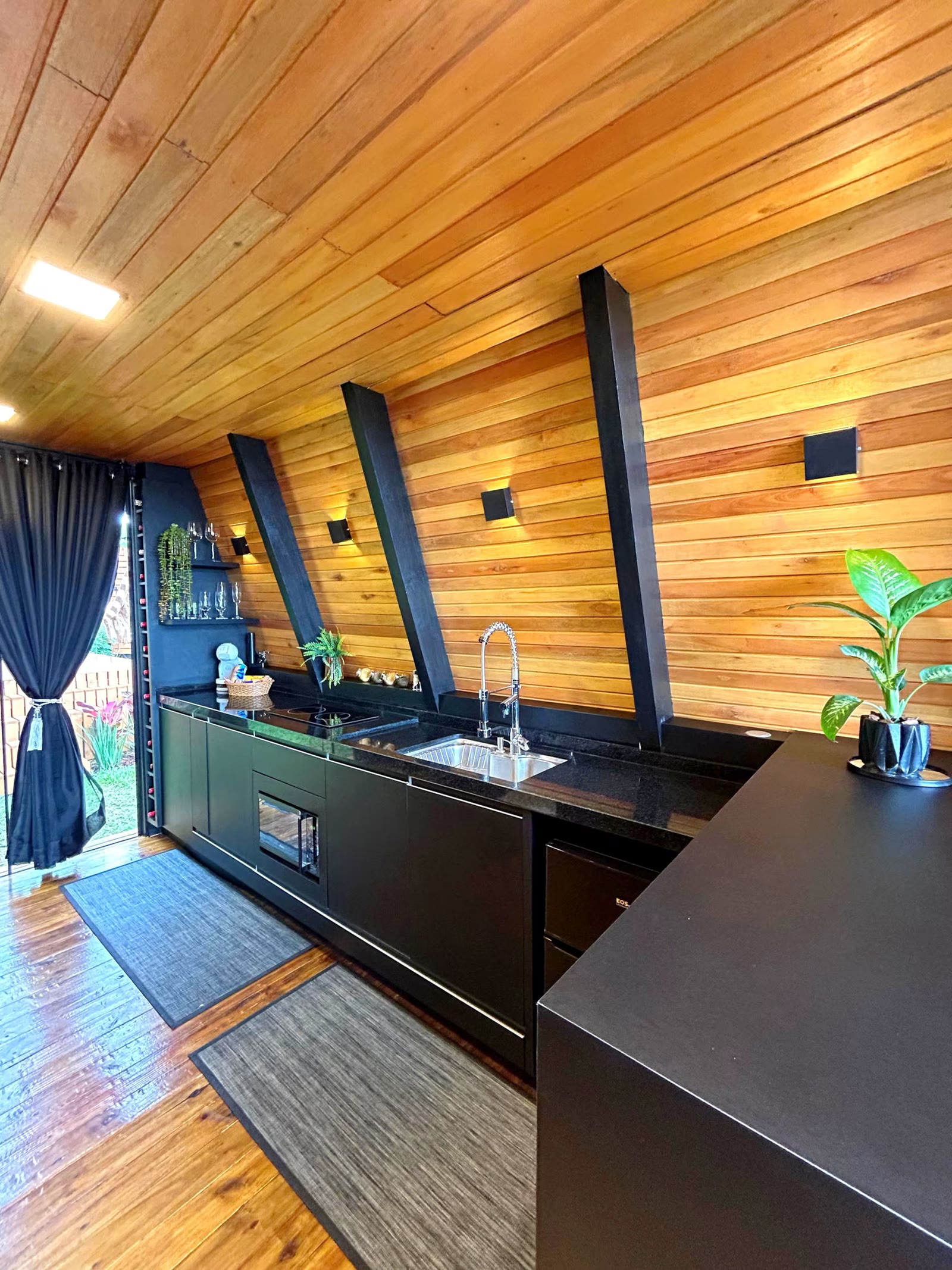 Cozinha do chalé com armários pretos, bancada e parede de madeira