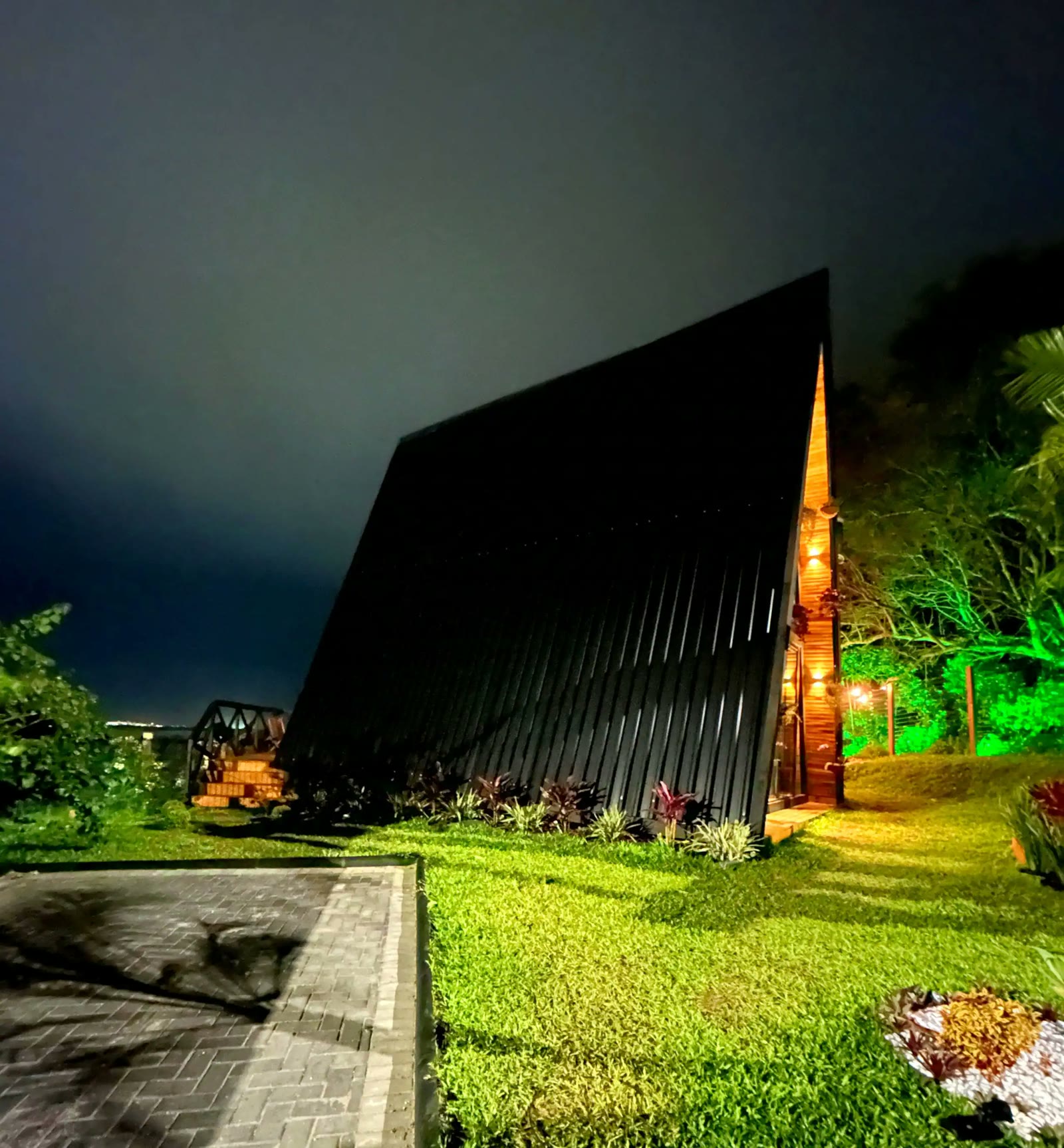 Fachada do chalé iluminada à noite, com o deck aceso