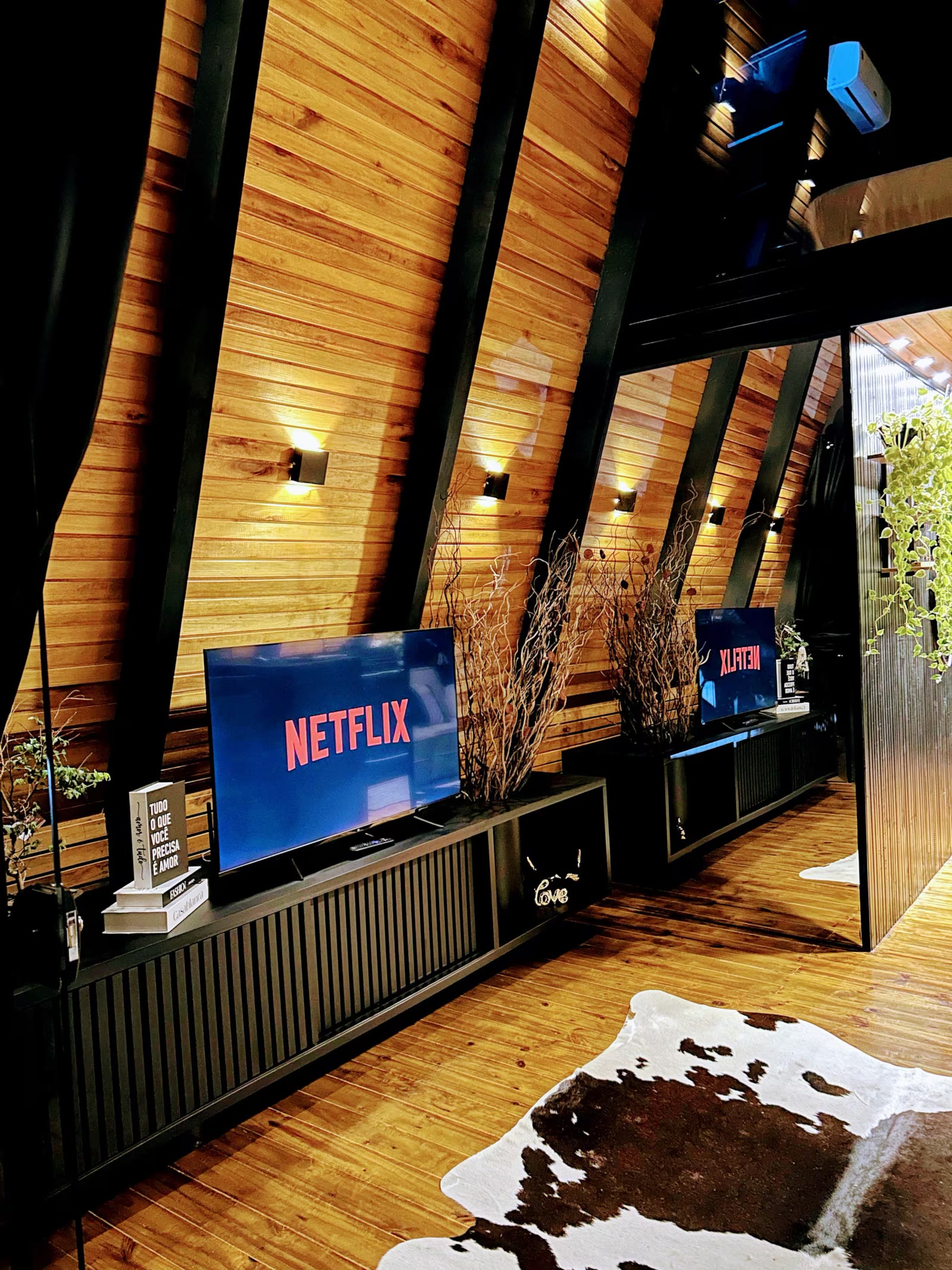 Sala com TV ligada na Netflix, parede de madeira e tapete de couro